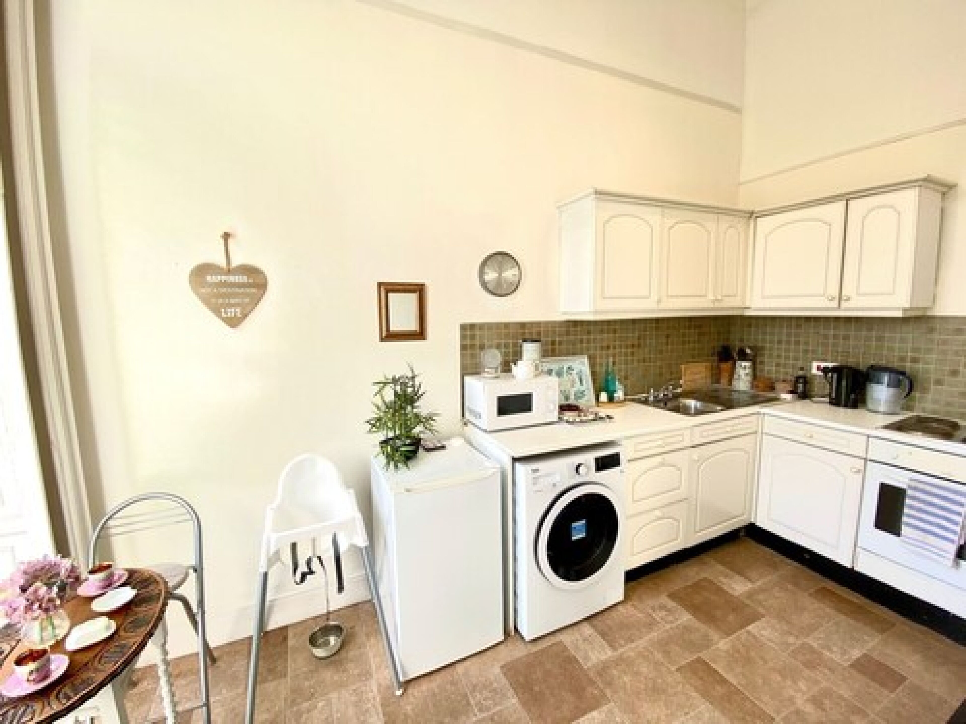 Cocina compacta con armarios blancos, lavadora, lavaplatos y comedor con mesa dispuesta para cuatro.
