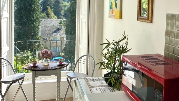 Eine Küche mit einem großen Fenster, einer roten Mikrowelle, einem Tisch mit Stühlen und einem Blumentopf.