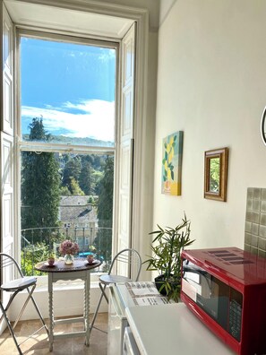 A kitchen with a large window, a red microwave, a table with chairs, and a potted plant. - Grosvenor Apartments (Bath)