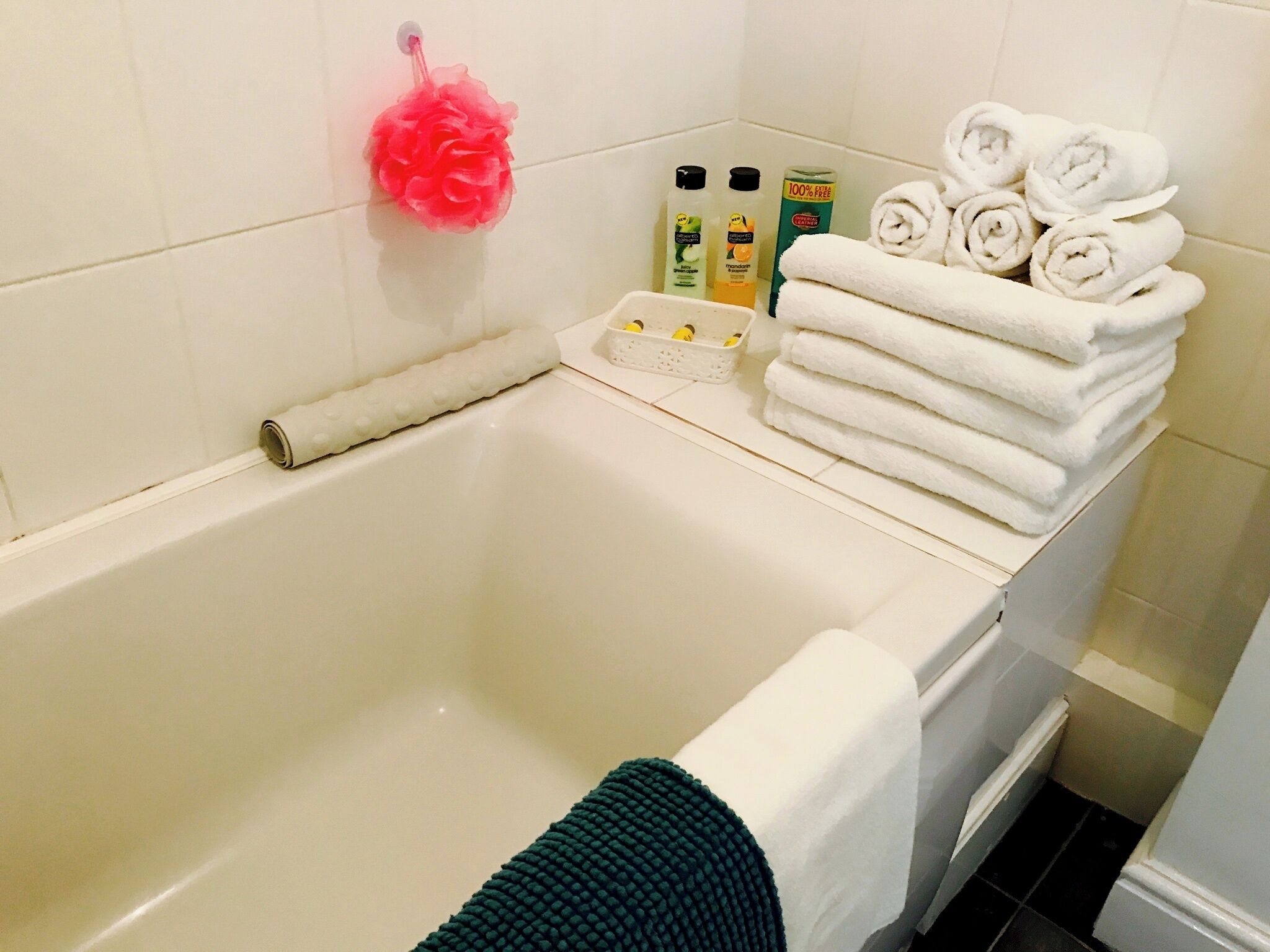 Un baño con una bañera, una pila de toallas blancas y artículos de aseo a un lado.