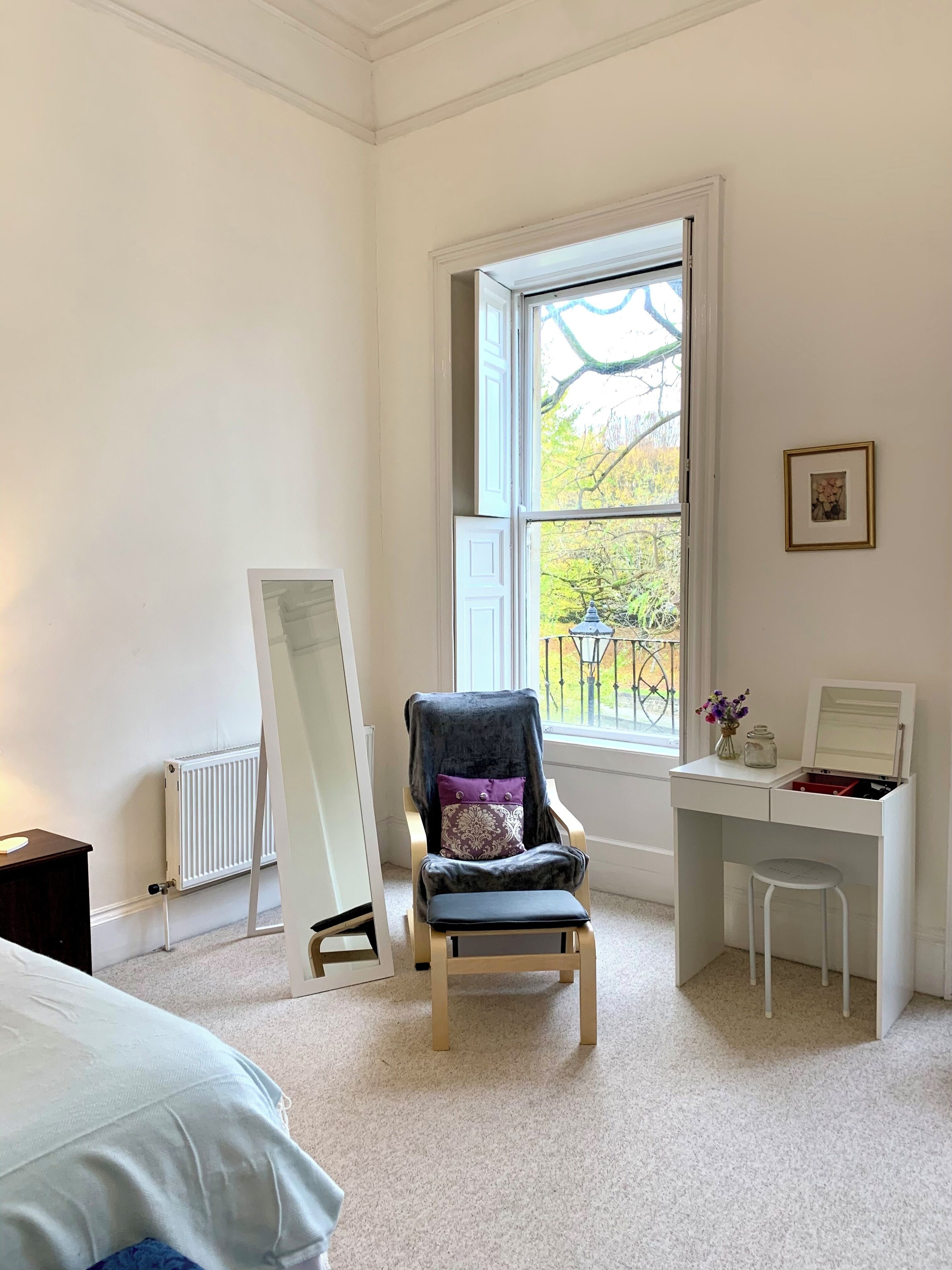 A bedroom with a bed, a desk, a chair, a radiator, and a window with a view of trees.