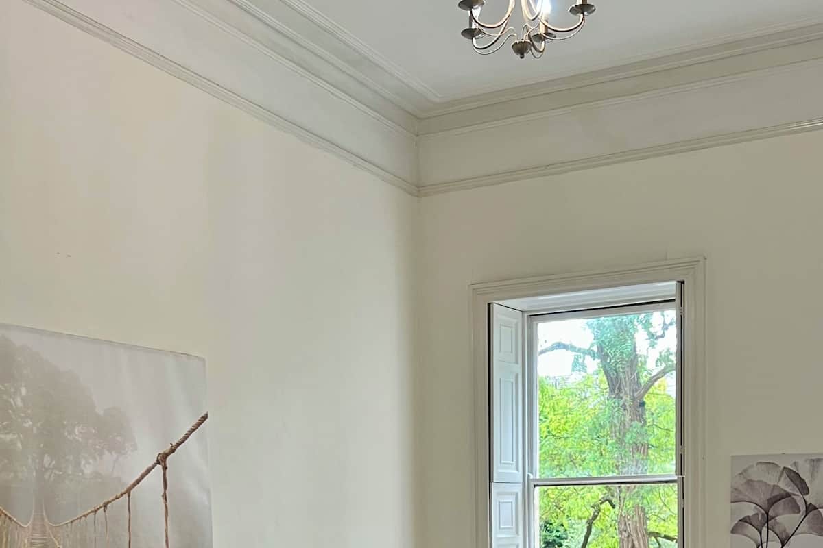 Quarto com uma cama grande, uma cadeira, uma escrivaninha e uma janela com vista para o verde.