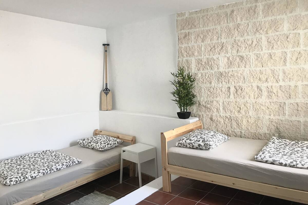 A small, cozy room with two wooden bunk beds, a small white table, a potted plant, and a wall with a textured stone pattern.