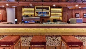 A bar area with wooden shelves displaying glasses and bottles, a counter with stools, and a stone wall in the background.