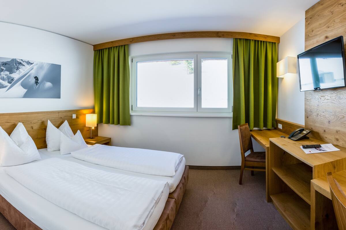 A hotel room with two beds, a desk, a chair, a TV, a window with curtains, and a picture on the wall.