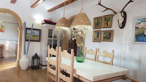 A dining area with a wooden table and chairs, a hanging woven light fixture, and wall-mounted artwork including a skull and framed paintings.