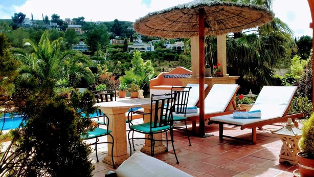 A patio with a pool, lounge chairs, a table, and a thatched umbrella.