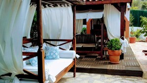 A wooden four-poster bed with white curtains, a blue patterned pillow, and a small potted plant beside it.