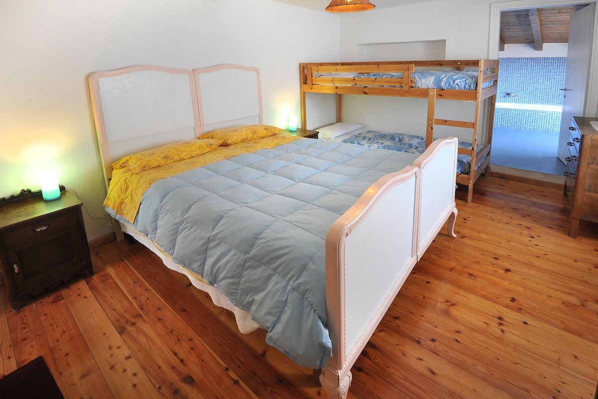 A bedroom with a bunk bed, a bedside table with a lamp, and a wooden floor.