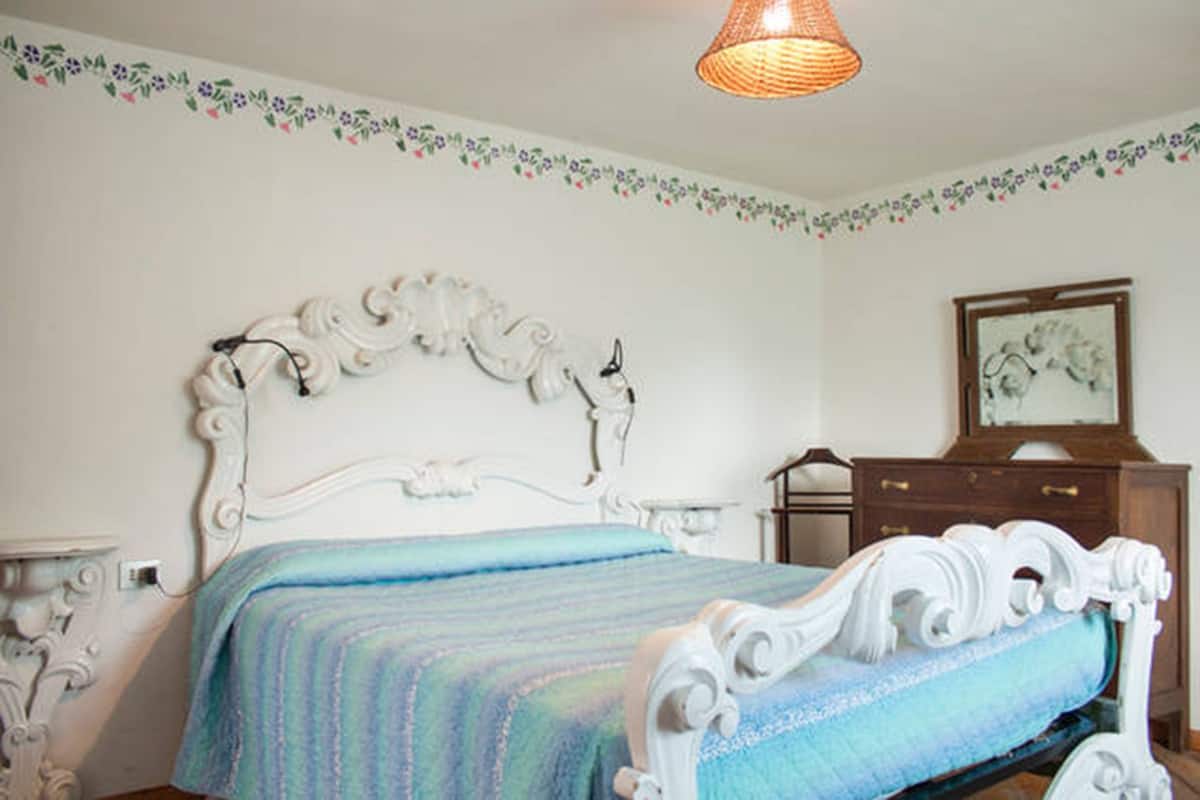 A bedroom with a white ornate bed frame, a blue striped bedspread, a wooden dresser, and a hanging lamp.
