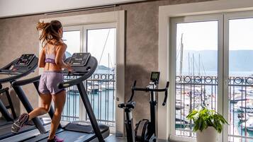Una mujer corre en una cinta de correr con vista a un puerto deportivo a través de amplias ventanas.