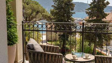 A balcony with wicker furniture, a table with a cup and saucer, and a view of the sea and hills.