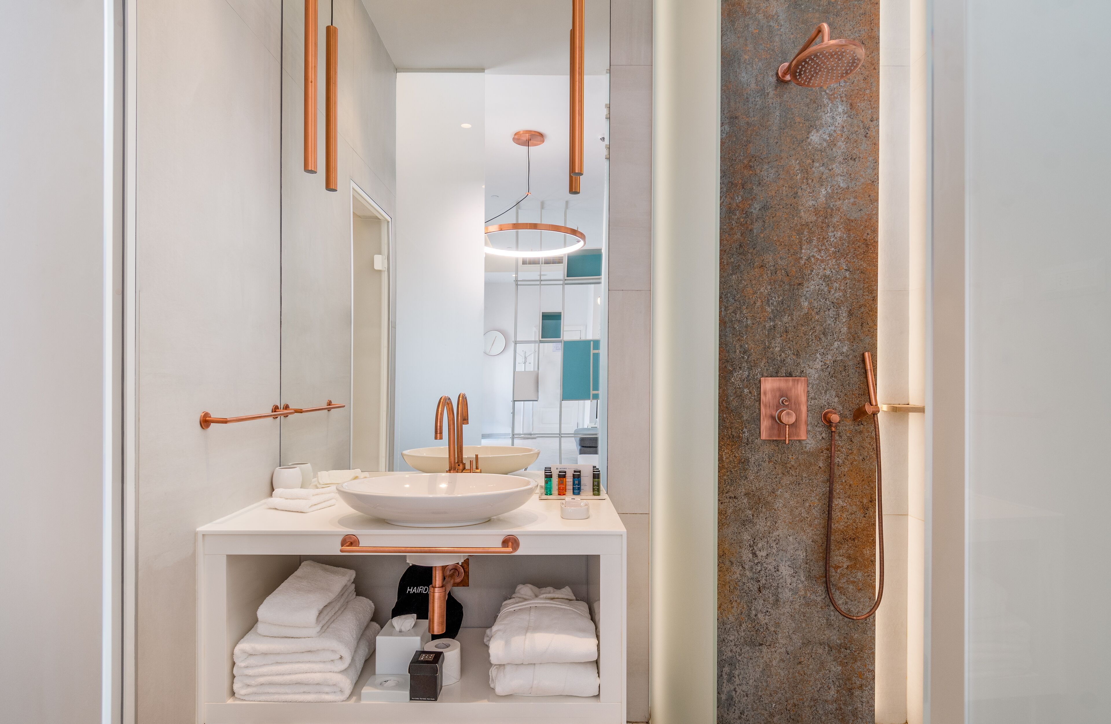 A modern bathroom with a white sink, copper fixtures, and a large mirror.