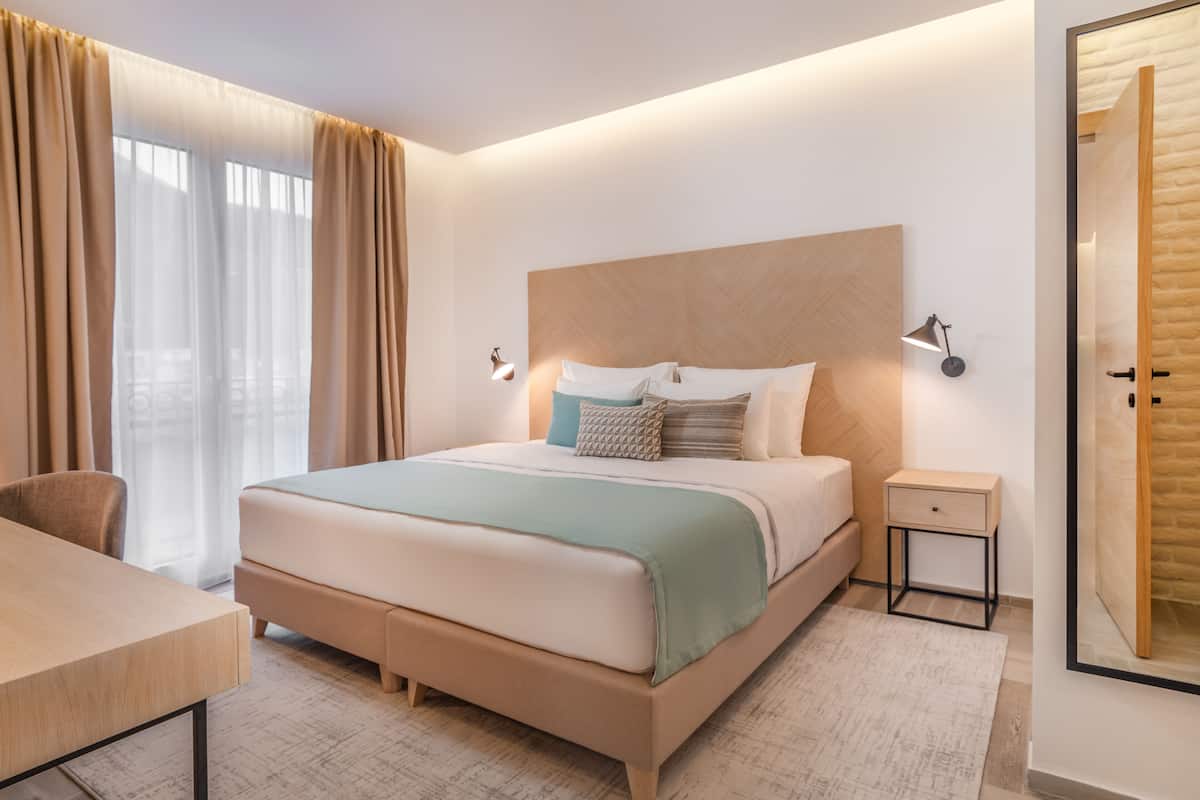 Ein modernes Hotelzimmer mit einem großen Bett, Nachttischen, einem Schreibtisch und Blick auf die Stadt.