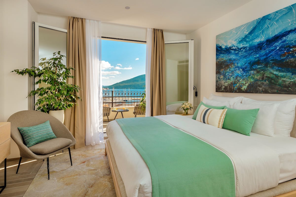 Ein Hotelzimmer mit Bett, Sessel, Pflanze und Balkon mit Aussicht.
