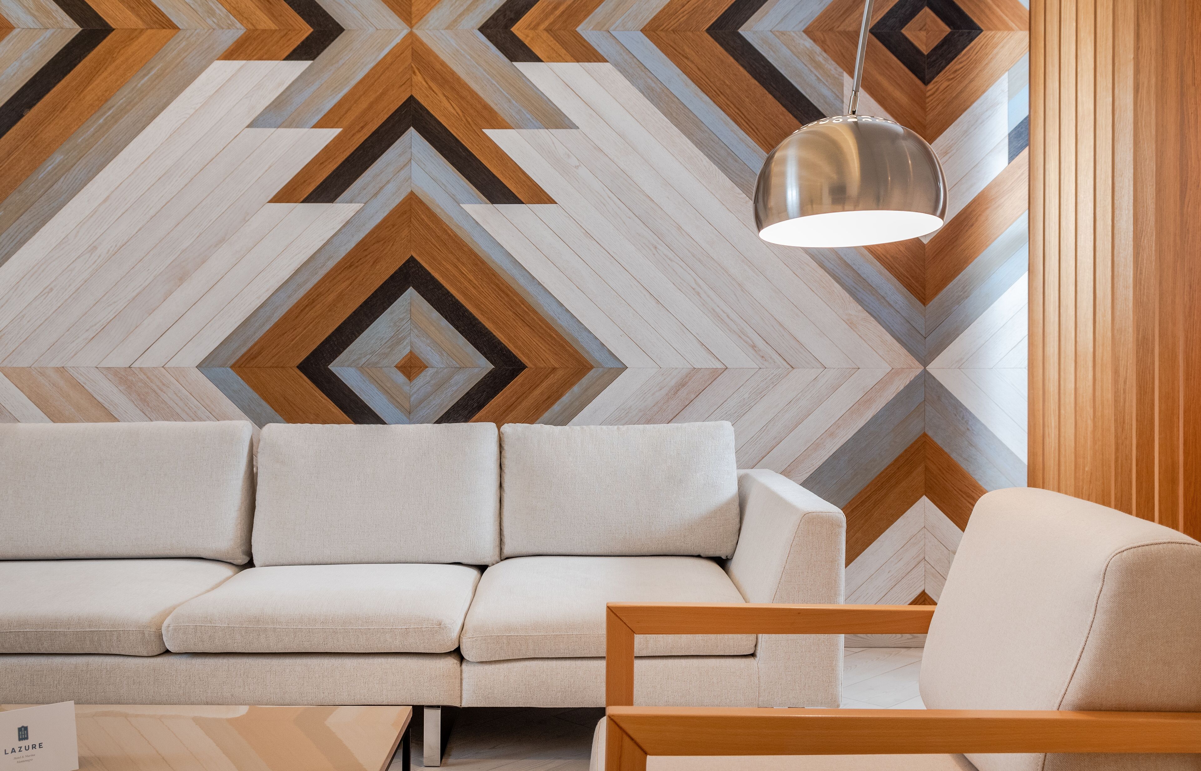 A modern living room with a geometric patterned wall, a sofa, a wooden side table, and a hanging pendant light.