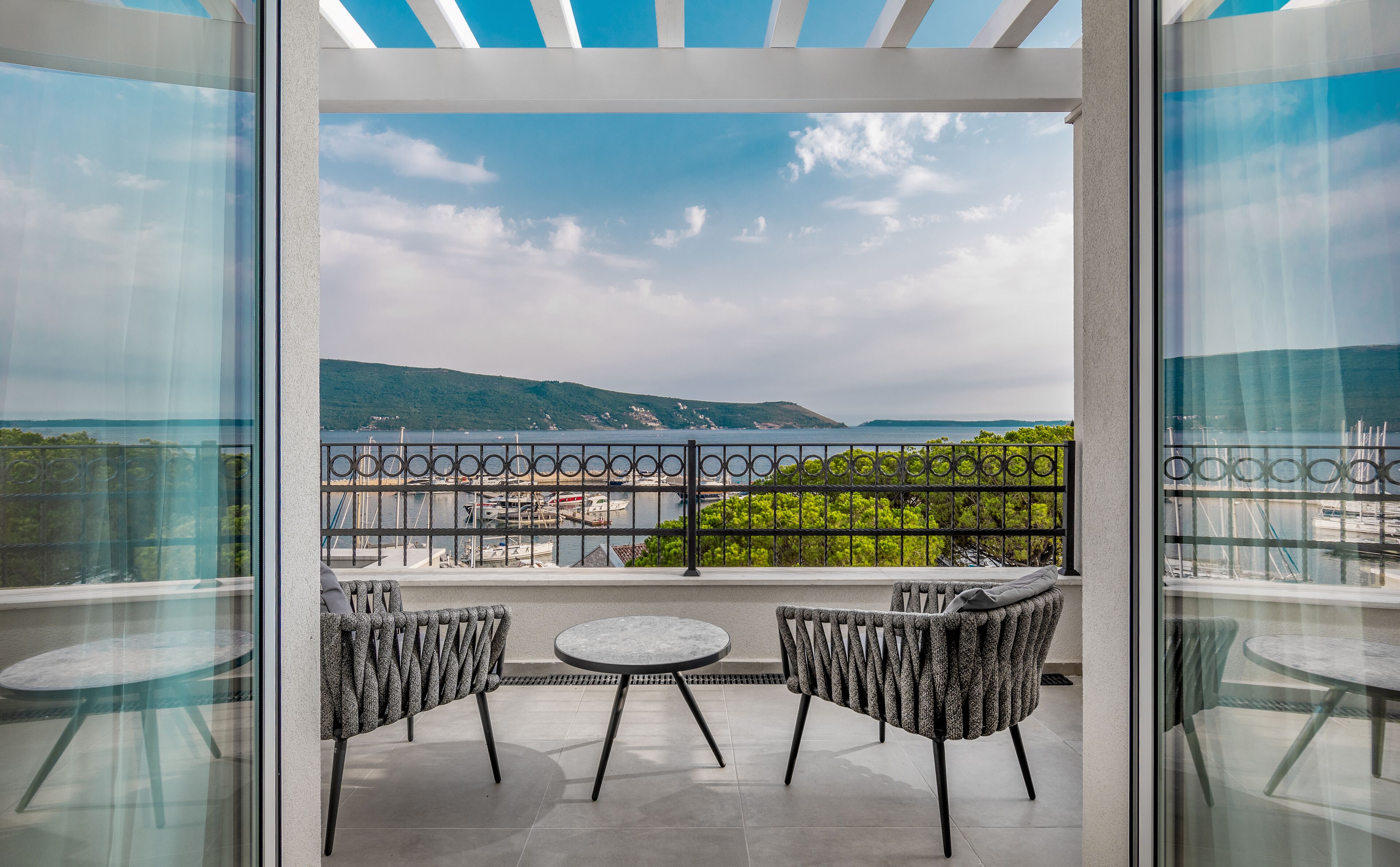 Ein Balkon mit zwei Stühlen und einem Tisch mit Blick auf einen Hafen und Hügel.