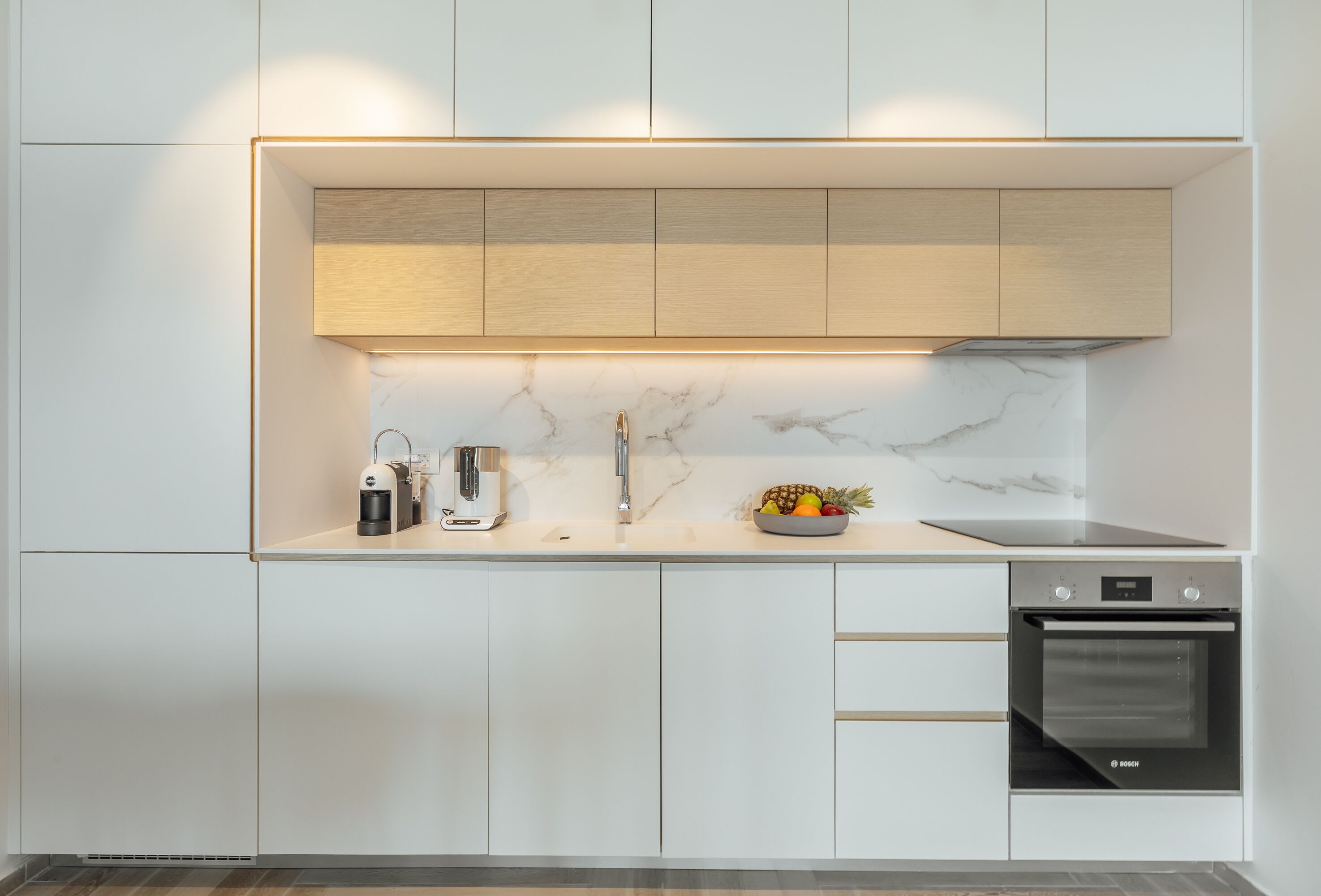 Cozinha moderna com armários brancos, forno Bosch e painel de mármore.