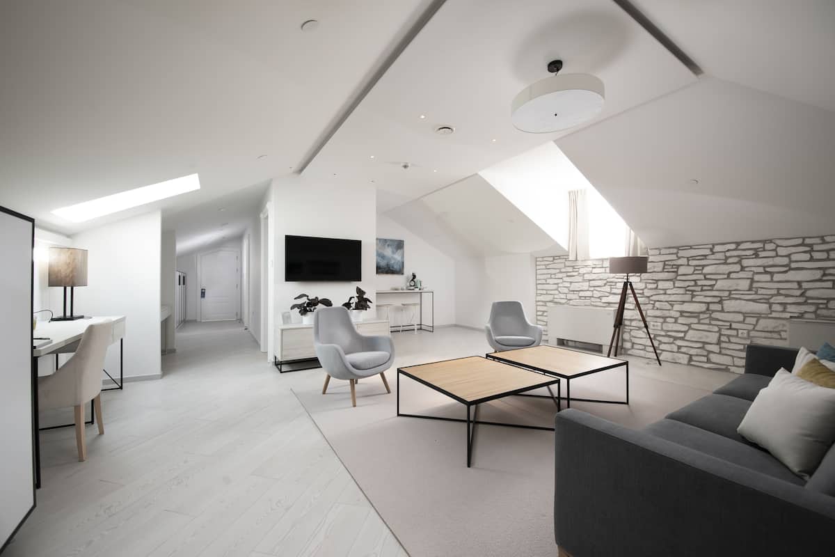 Eine moderne Lofts-Wohnung mit hohen Decken, einer Wand aus Stein, einem Essbereich mit Tisch und Stühlen, einem Wohnzimmer mit Sofa und Couchtisch sowie einem an der Wand montierten Fernseher.