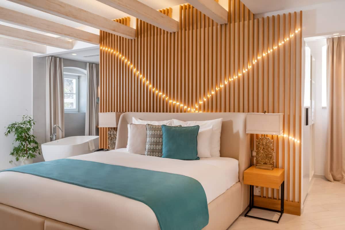 Ein modernes Hotelzimmer mit einem großen Bett, einem Nachttisch mit Lampe, einer dekorativen Wandverkleidung und Blick nach außen.