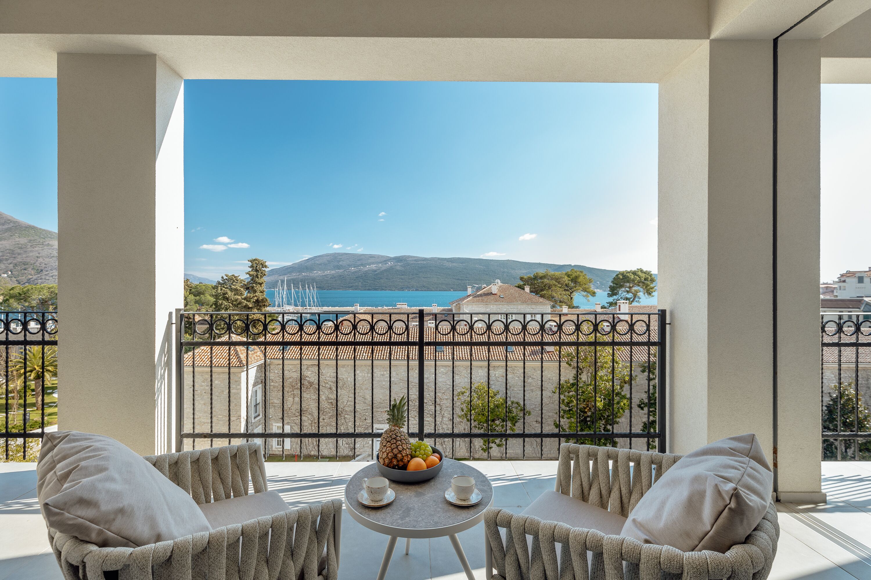 Ein Balkon mit Tisch und zwei Stühlen, einer Obstschale und Blick auf eine gebirgige Landschaft.