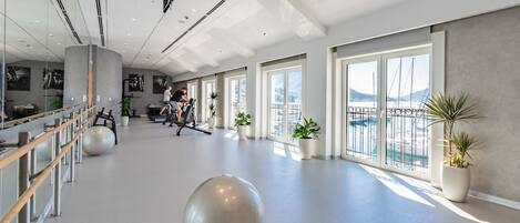A spacious indoor area with exercise bikes, large potted plants, and a view of a marina through large windows.