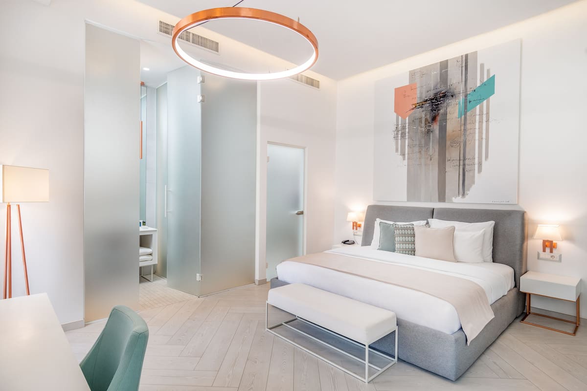 Ein modernes Schlafzimmer mit einem großen Bett, Nachttischen, einer Bank und einem an der Wand befestigten Kunstwerk.
