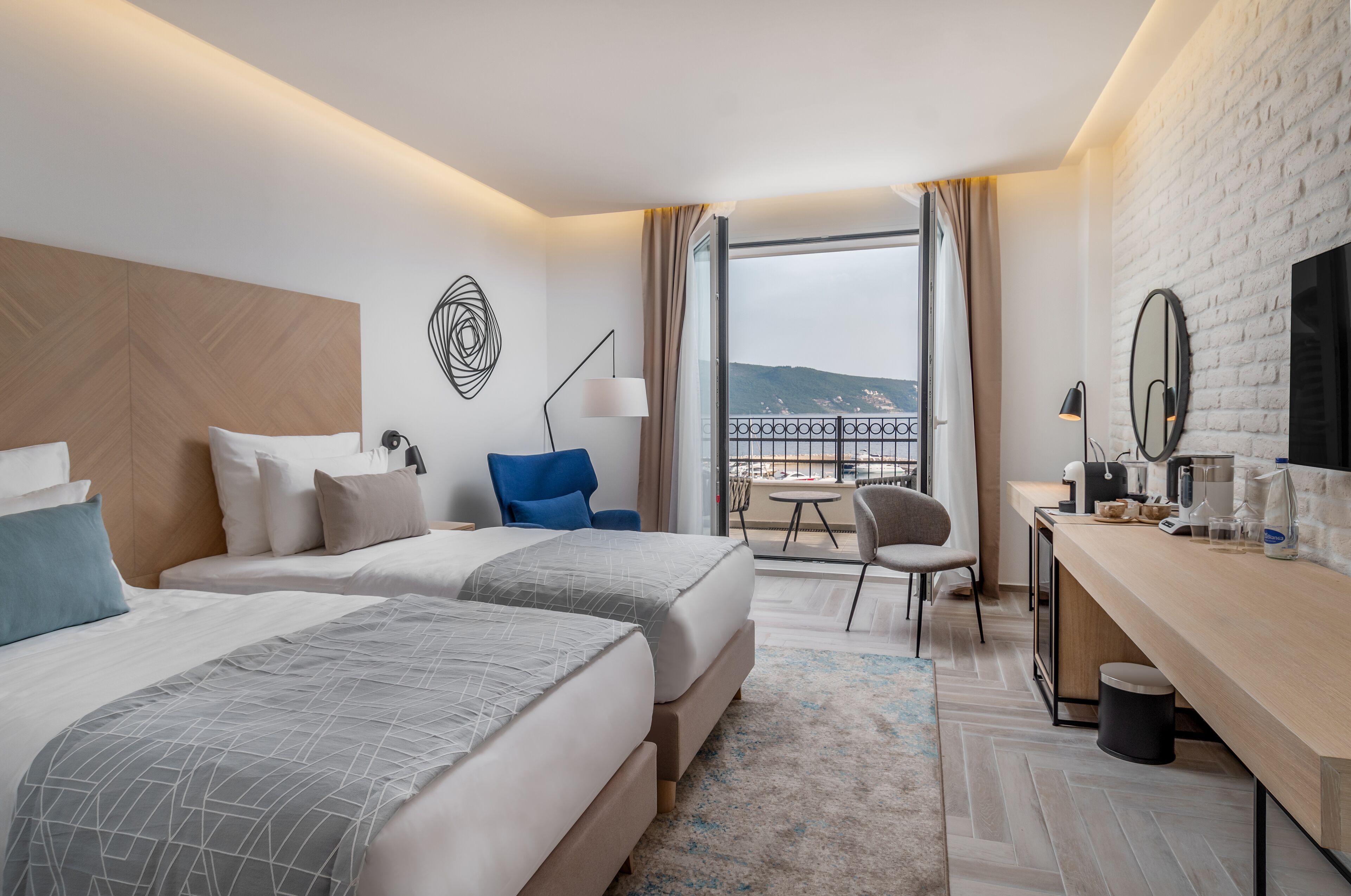 Habitación de hotel con dos camas, un escritorio, una silla, un televisor y un balcón con vistas.