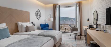 Habitación de hotel con dos camas, un escritorio, una silla, un televisor y un balcón con vistas.
