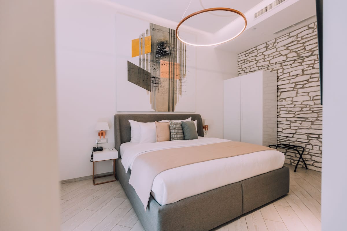 Ein modernes Schlafzimmer mit einem großen Bett, einem Nachttisch, einem an der Wand befestigten abstrakten Kunstwerk und einer Steinwand.