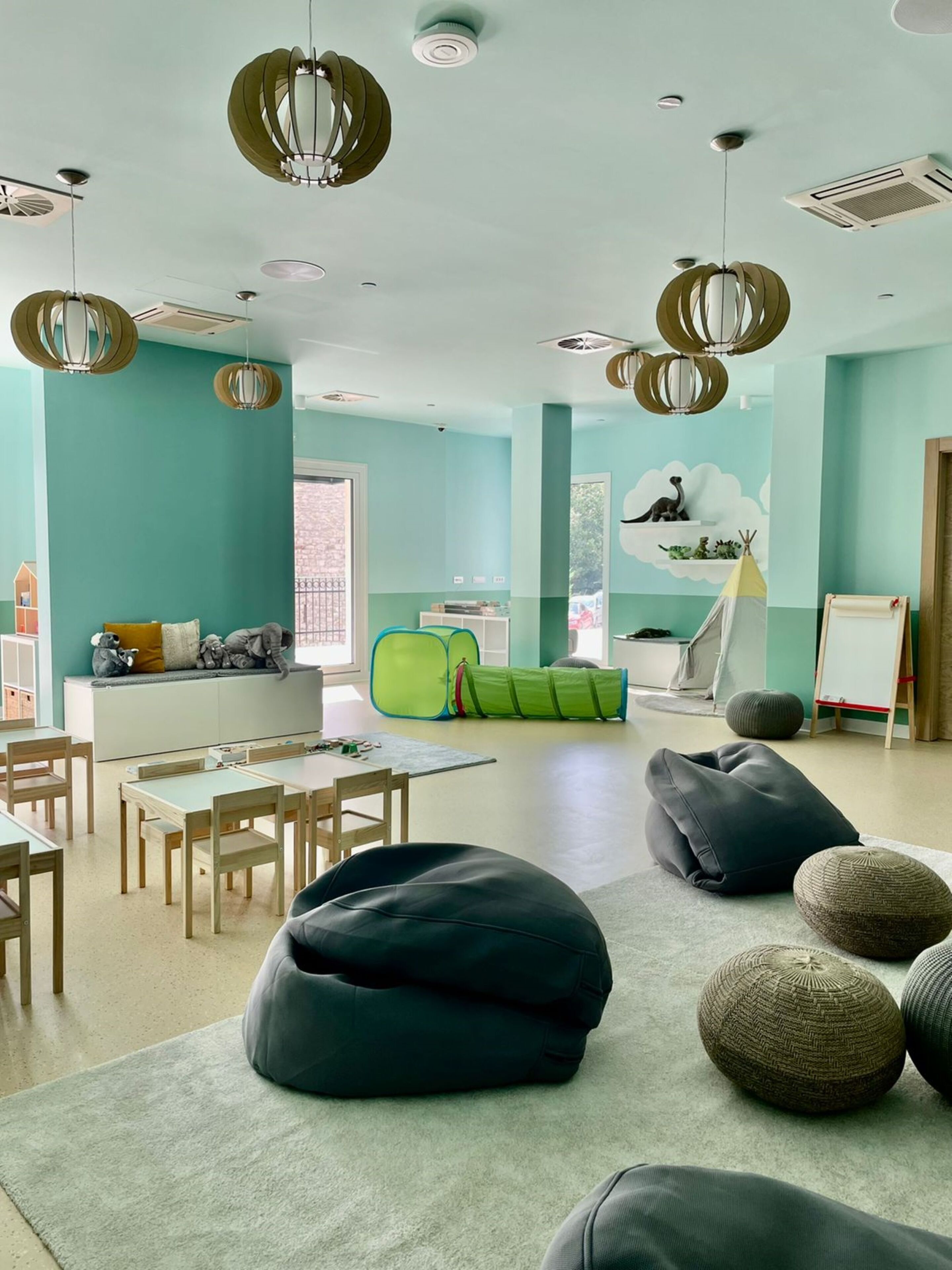 A spacious room with teal walls, a large window, and a play area with a green tent and toys.