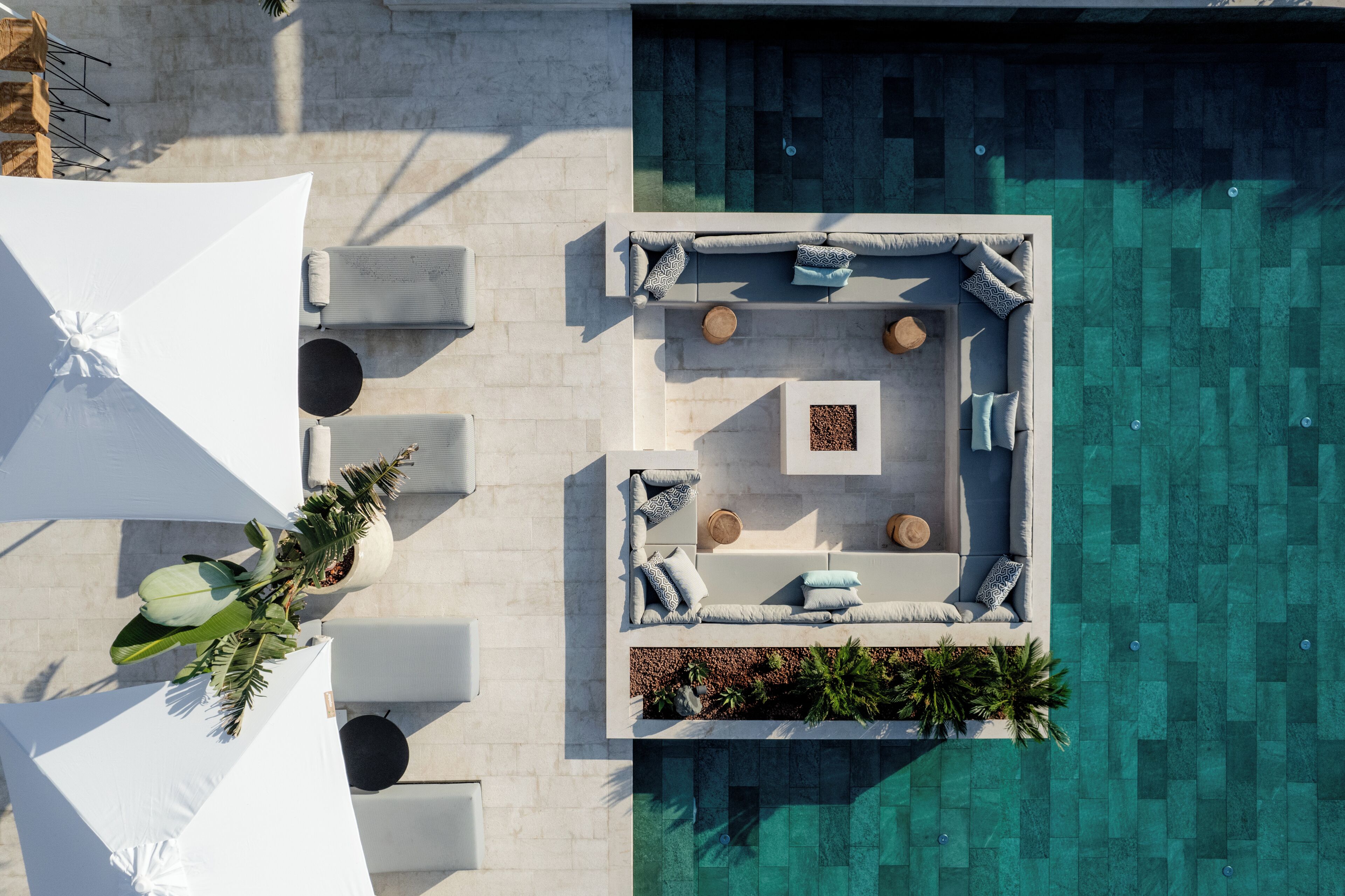 An aerial view of a pool area with a seating arrangement, umbrellas, and a planter with tropical plants.