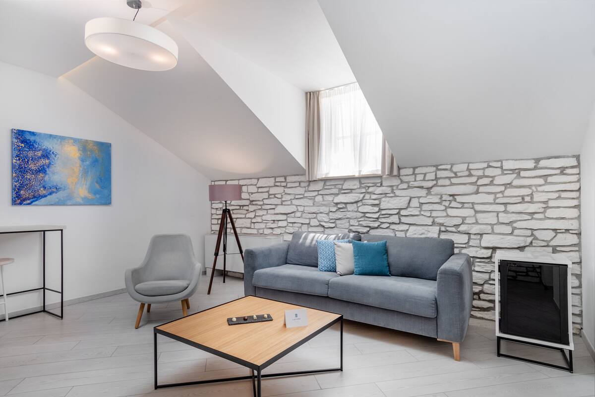 Ein modernes Wohnzimmer mit einer Steinwand, einem grauen Sofa mit blauen und weißen Kissen, einem grauen Sessel, einem Holztisch und einem kleinen Beistelltisch.