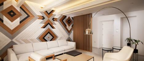 A modern living room with a white sofa, a wooden coffee table, a white armchair, and a geometric-patterned wall.