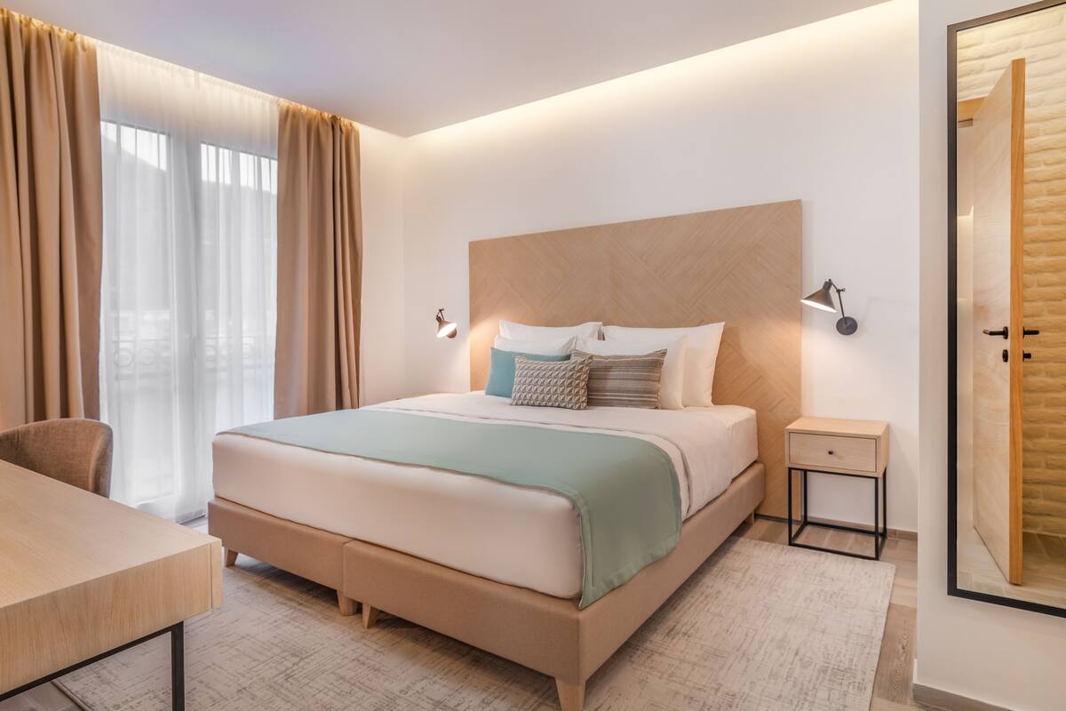 Ein modernes Hotelzimmer mit einem großen Bett, Nachttischen, einem Schreibtisch und Blick auf die Stadt.