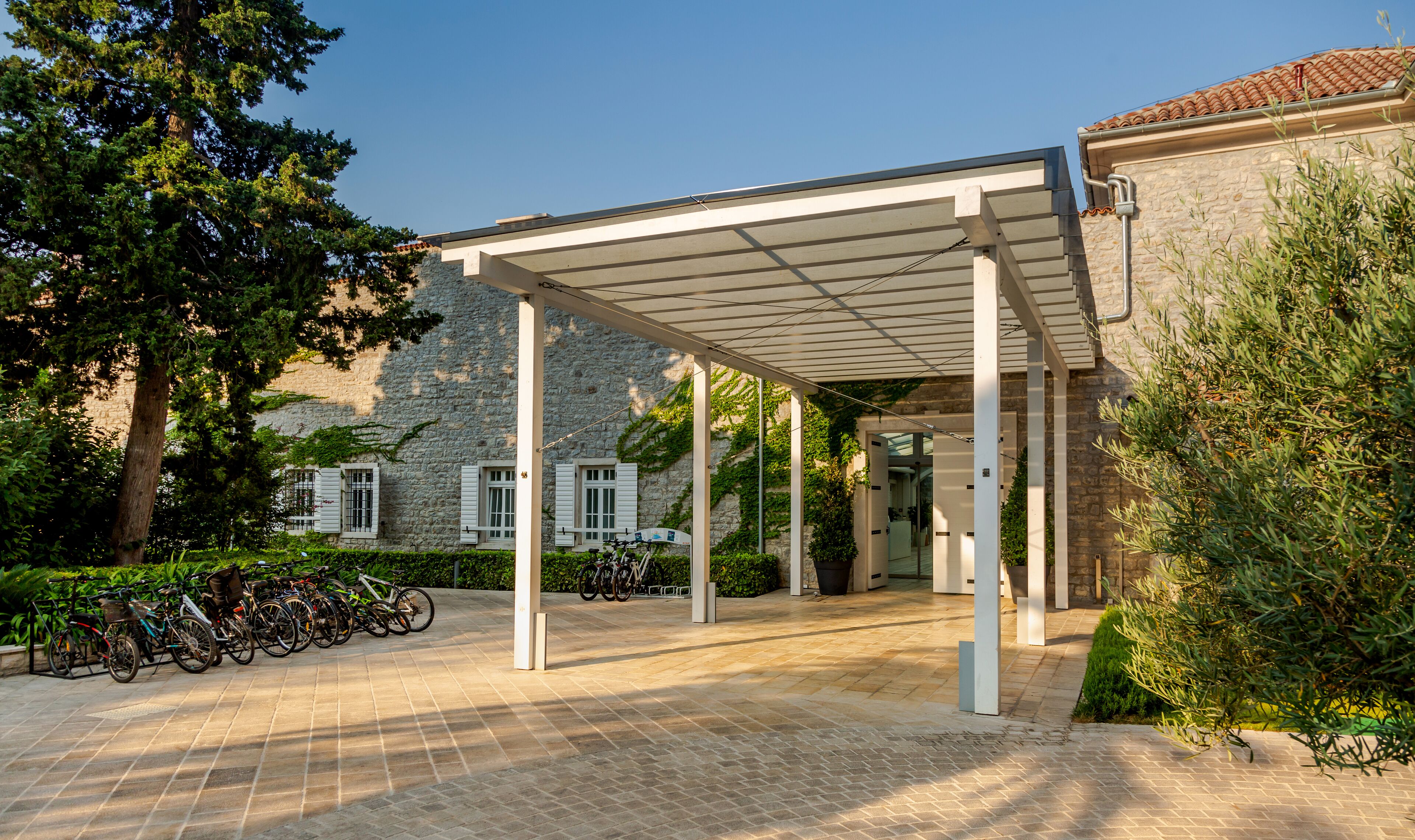 A covered outdoor area with a stone building in the background, bicycles parked, and a clear sky.