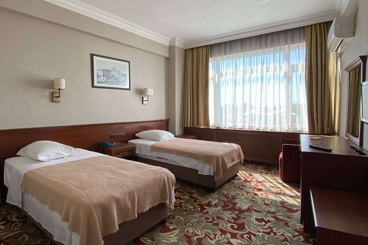 A hotel room with two beds, a desk, and a large window with curtains.