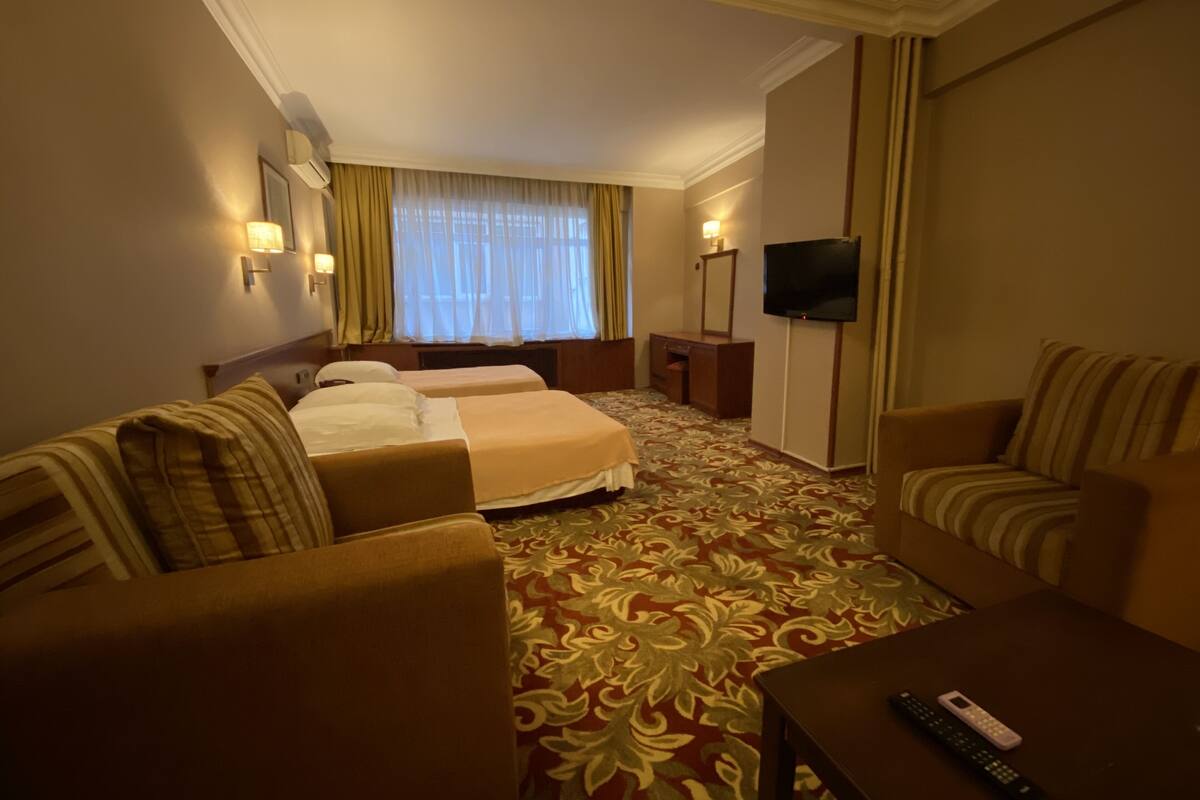 A hotel room with a bed, two armchairs, a sofa, a TV, and a carpeted floor.