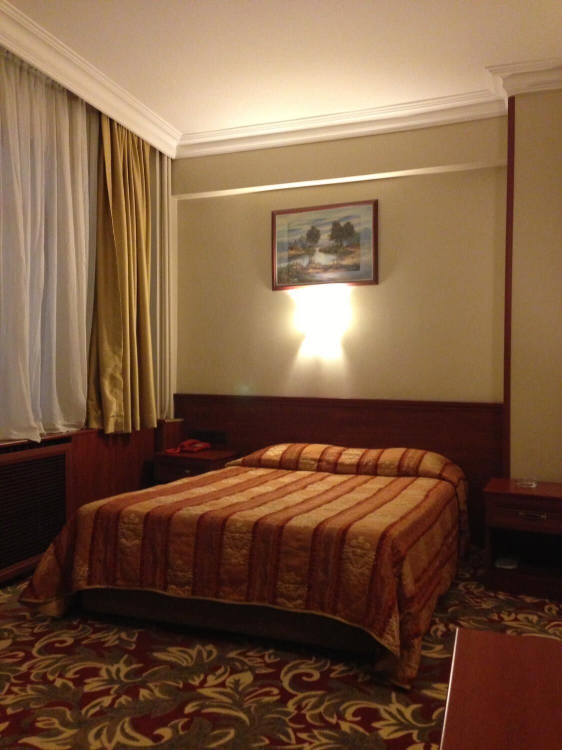 A hotel room with a large bed, a nightstand, a lamp, and a painting on the wall.
