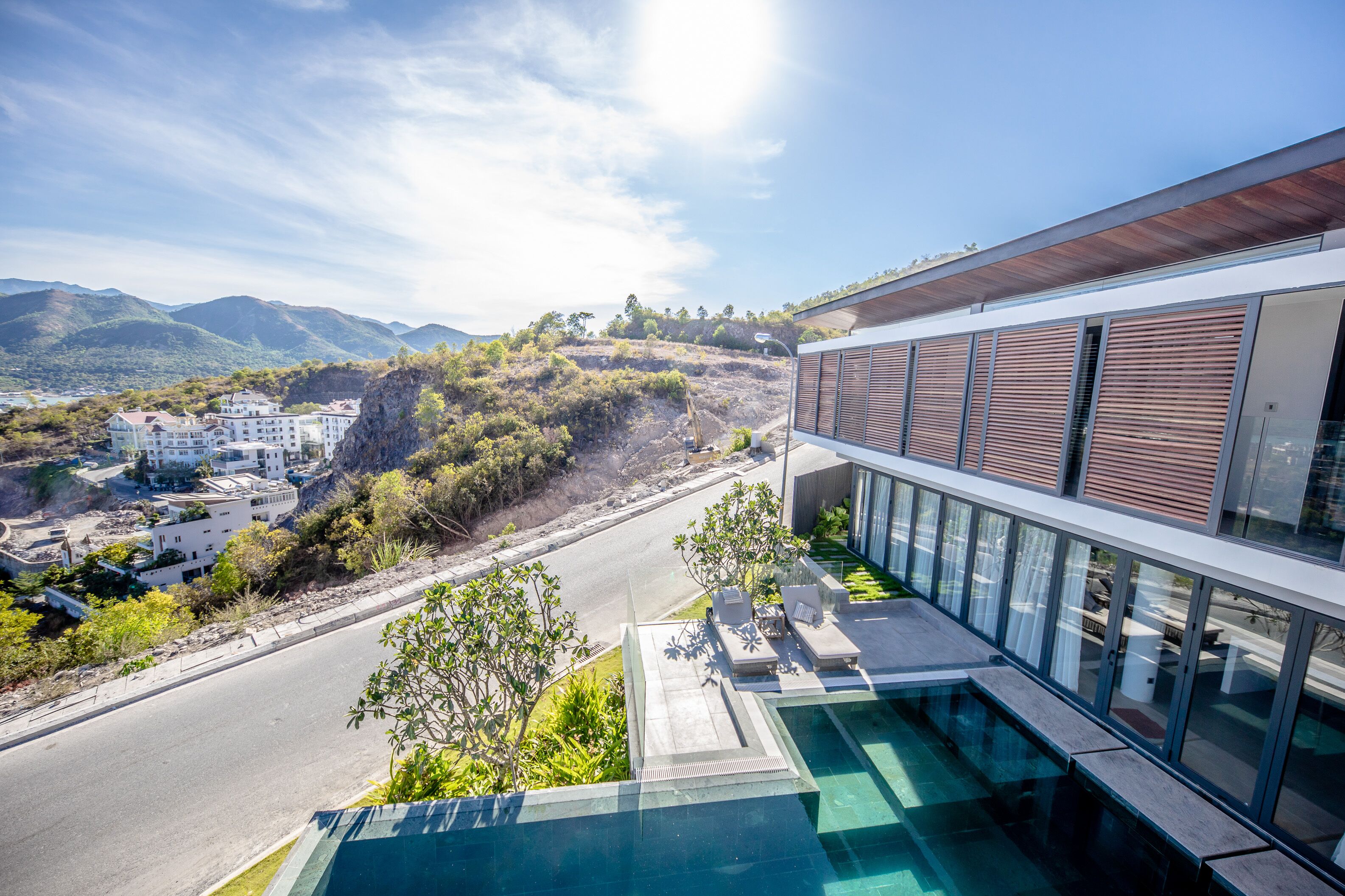 A modern building with a swimming pool, overlooking a road and hills.