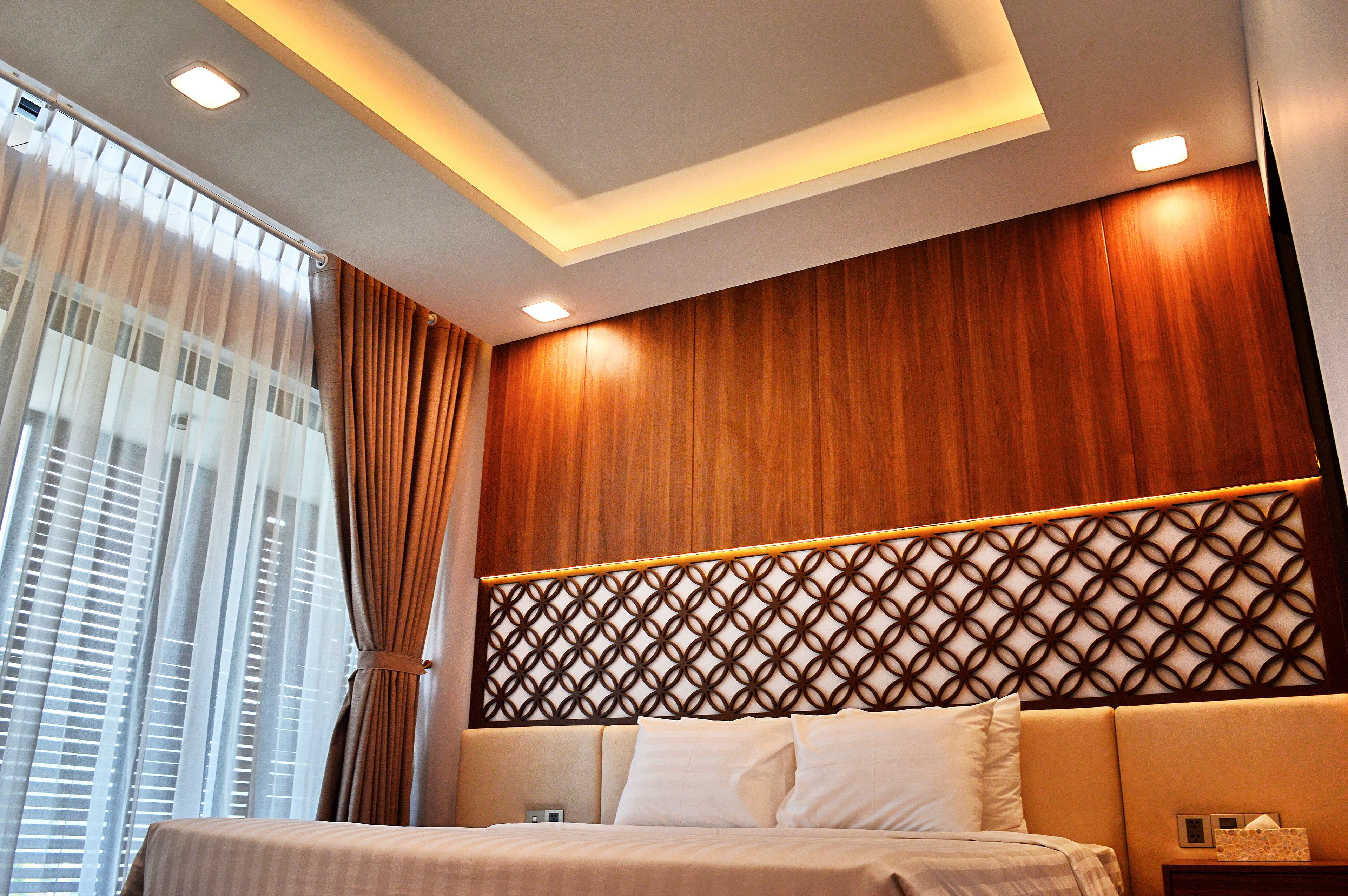 A modern hotel room with a large bed, wooden paneling on the wall, and a decorative headboard.