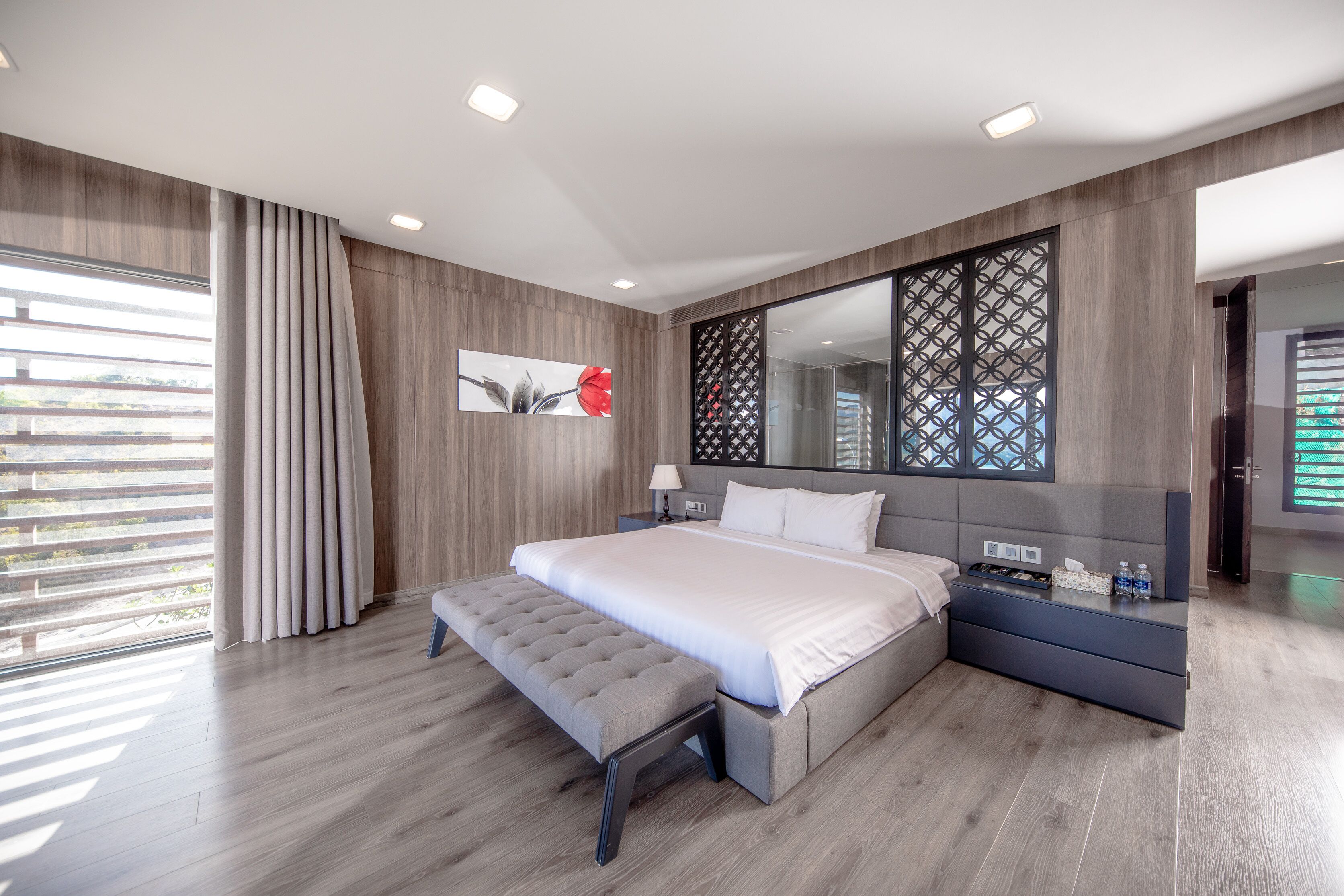 A modern bedroom with a large bed, a bench, a bedside table, and a decorative mirror.