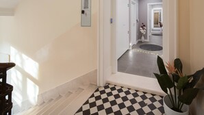 A hallway with a checkered floor, a potted plant, and a door leading to another room.