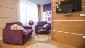 A modern living room with two purple sofas, a flat-screen TV mounted on a wooden wall, and a small round coffee table.