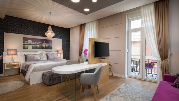 A modern bedroom with a bed, bedside tables, a TV, a desk, and a balcony.