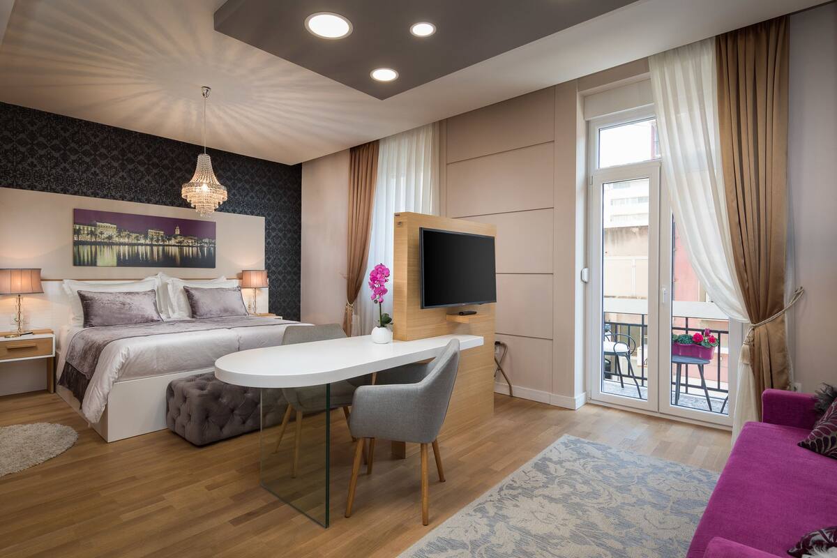 A modern bedroom with a bed, bedside tables, a TV, a desk, and a balcony.