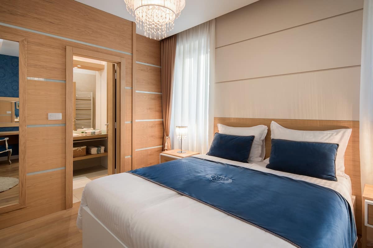 A modern hotel room with a large bed, wooden wardrobe, and a chandelier.