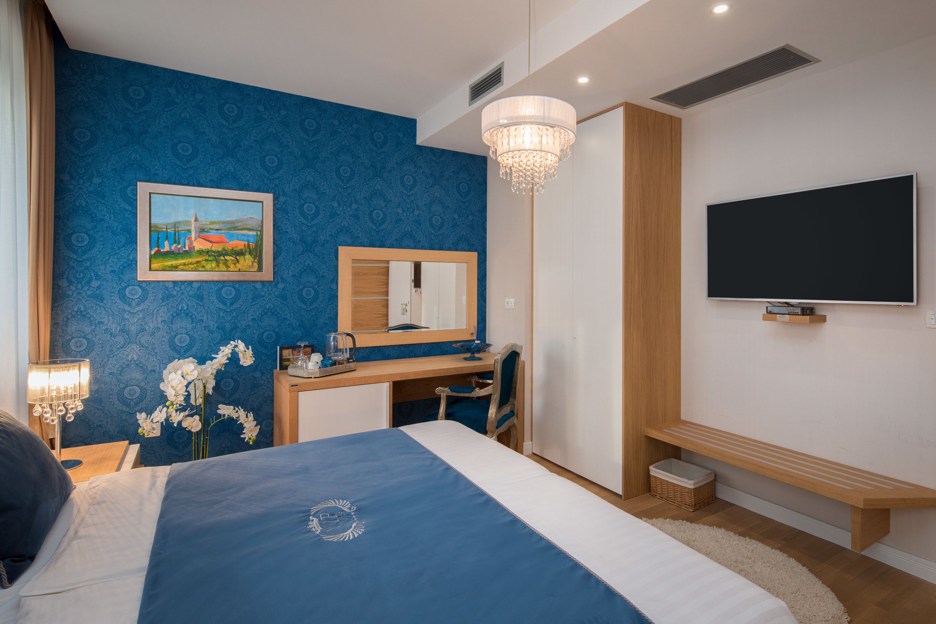 Une chambre à coucher comprenant un lit, un bureau, une chaise, une télévision, un miroir et un lustre.