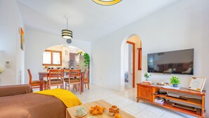 Una sala de estar moderna con sofá, mesa de centro, televisor y un comedor con sillas y una mesa.