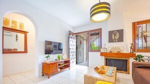 Una sala de estar con televisión, muebles de madera, chimenea y un cojín amarillo.